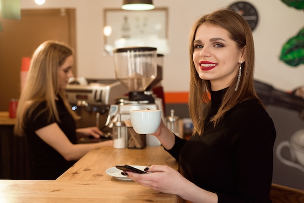 Lächelnde Frau in einer guten Laune genießen den Tasse Kaffee, der in einem Café sitzt.