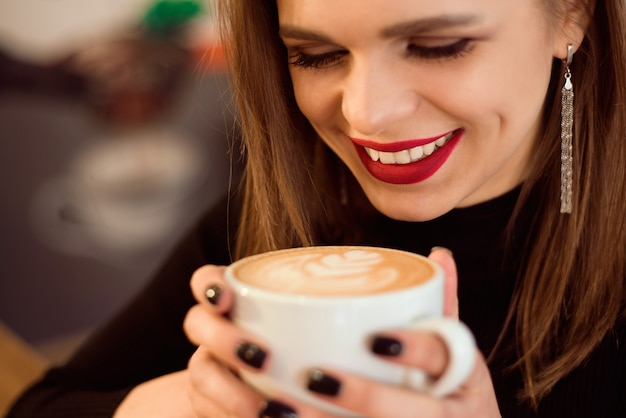 Lächelnde Frau in einer guten Laune genießen den Tasse Kaffee, der in einem Café sitzt.