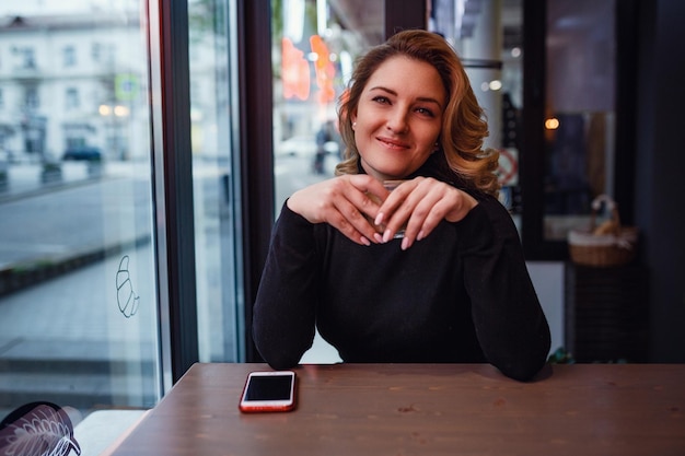 Lächelnde Frau in einer guten Stimmung mit einer Tasse Kaffee, die in Cafés sitzt, dunkle Innenräume, Abendversammlungen in einem Café