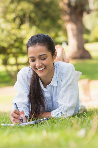 Lächelnde Frau mit Buch und Stift im Park