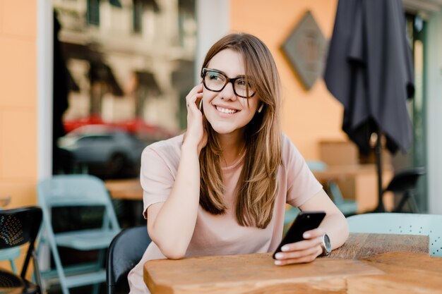 Lächelnde Frau mit einem Telefon, das im Café sitzt