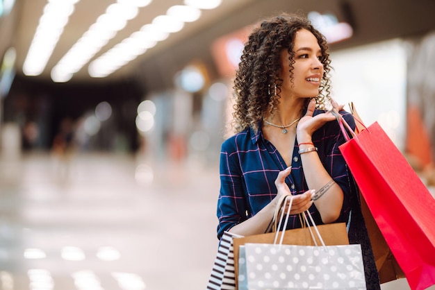 Lächelnde Frau mit Einkaufstüten, die den Einkauf im Einkaufszentrum genießenJunge Frau mit Paketen nach dem Einkauf