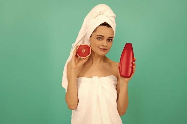 Lächelnde Frau mit Grapefruit-Shampooflasche auf blauem Hintergrund