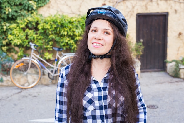 Lächelnde Frau mit Helmposition auf Hintergrundfahrrad und Gasse