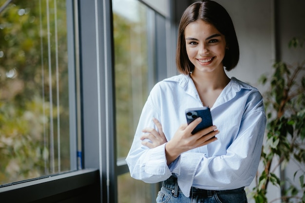 Lächelnde Frau mit ihrem Telefon in einem Büro Unternehmensperson lächelt mit einem Telefon in den Händen