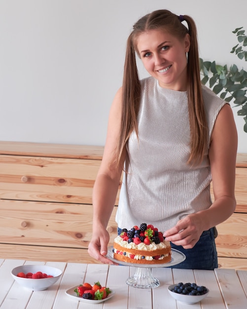 Lächelnde Frau mit langen Haaren im Schwanz verziert Kuchen mit Beeren