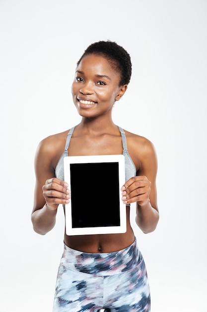 Lächelnde Frau mit leerem Tablet-Computerbildschirm isoliert auf einer weißen Wand