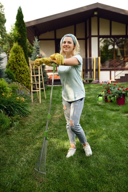 Lächelnde Frau mit Rechen arbeitet im Garten