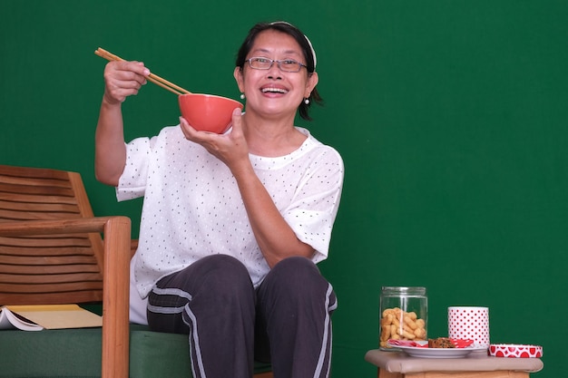 Lächelnde Frau mit Schüssel und Essstäbchen Snacks und Buch neben ihr