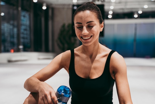Lächelnde Frau mit Wasserflasche sitzt im Fitnessstudio