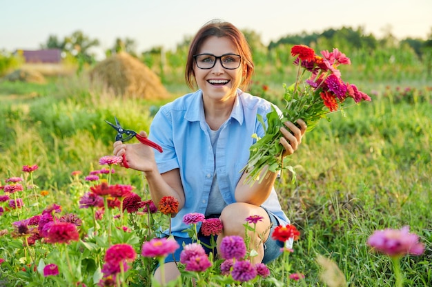 Lächelnde Frau mittleren Alters, die einen Strauß frischer Zinnia-Blumen im Garten hält