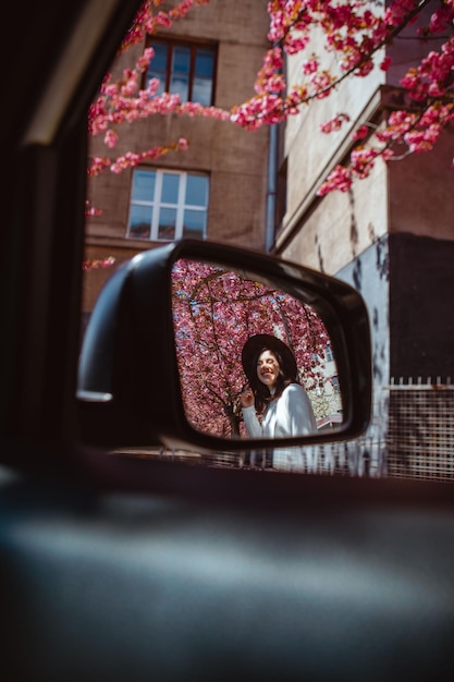 Lächelnde Frau Spiegelbild im Auto Rückspiegel blühender Sakura-Baum im Hintergrund Der Frühling kommt