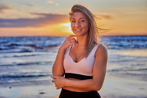 Lächelnde Frau steht während des Sonnenuntergangs an der Küste