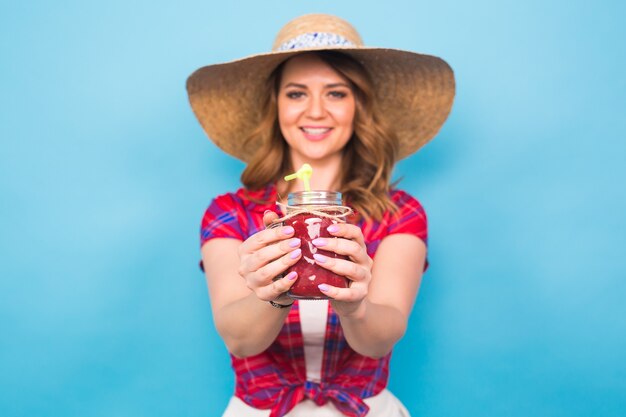 Lächelnde Frau trinken roten Saft. Studioportrait mit blauem Hintergrund und Kopienraum.