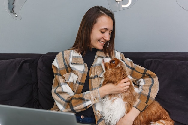 Lächelnde Frau umarmt Hund beim Sitzen auf dem Sofa während der Arbeitspause