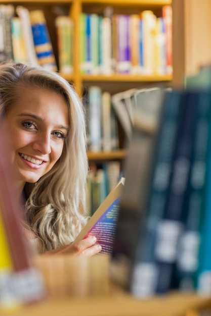 Lächelnde Frau unter Bücherregalen in der Bibliothek