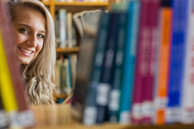 Lächelnde Frau unter Bücherregalen in der Collegebibliothek