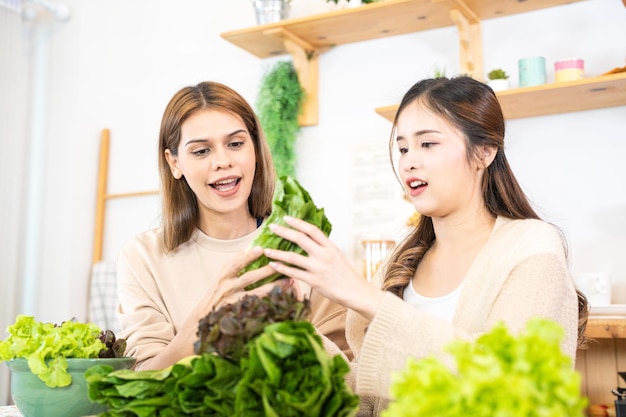 Lächelnde Frauen bereiten frisches, gesundes Salatgemüse zu. Frau sitzt in der Speisekammer in einer schönen Innenküche. Die saubere Diätkost aus lokalen Produkten und Zutaten. Marktfrisch