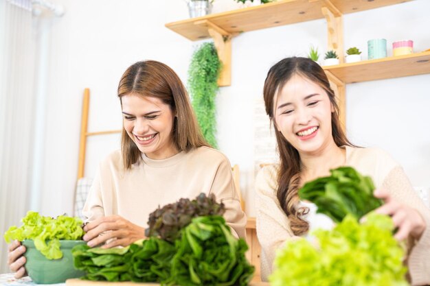 Lächelnde Frauen bereiten frisches, gesundes Salatgemüse zu. Frau sitzt in der Speisekammer in einer schönen Innenküche. Die saubere Diätkost aus lokalen Produkten und Zutaten. Marktfrisch