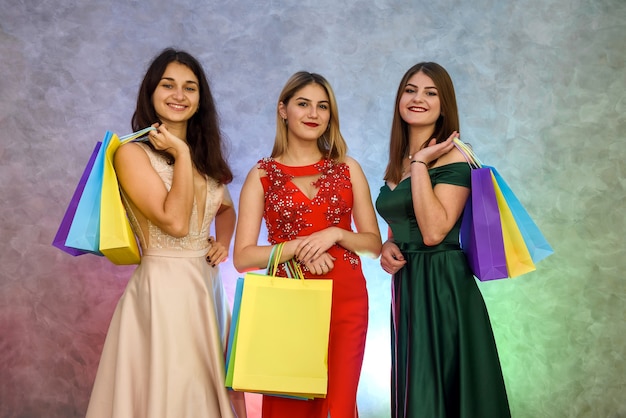 Lächelnde Frauen in eleganten Kleidern posieren mit Geschenktüten im Studio. Weihnachtsgeschenke