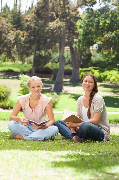 Lächelnde Frauen mit ihren Büchern, die im Park sitzen