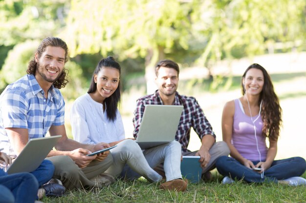 Lächelnde Freunde, die Mediengeräte im Park verwenden