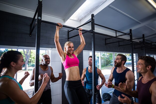 Lächelnde Freunde jubeln Frau, die Klimmzüge im Fitnessstudio tut