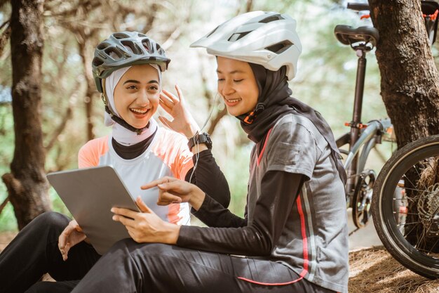 Lächelnde Freundinnen sitzen im Park und benutzen ein digitales Tablet