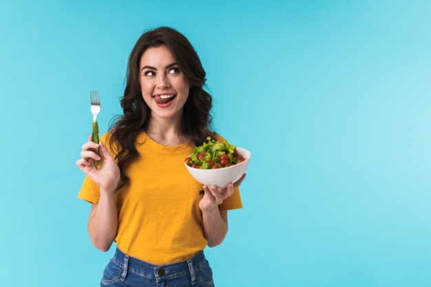 lächelnde fröhliche Frau posiert isoliert über blaue Wand mit Salat.