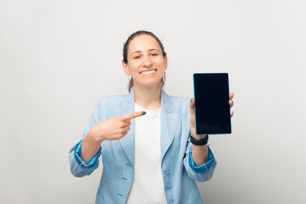 Lächelnde fröhliche Frau zeigt auf den Bildschirm des Tablets.