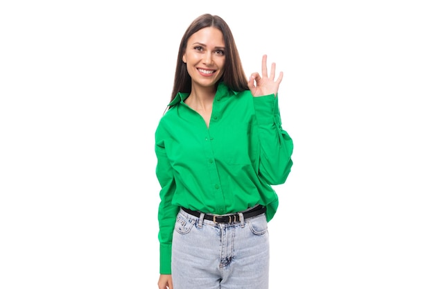 Lächelnde, fröhliche junge kaukasische brünette Dame mit Make-up, gekleidet in einem grünen Hemd und Jeans auf einem