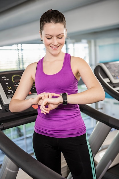 Lächelnde geeignete Frau, die smartwatch auf Tretmühle in der Turnhalle verwendet