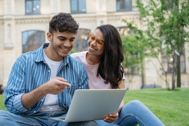Lächelnde gemischte Studenten mit Laptop, die zusammen im Park-Online-Bildungskonzept studieren