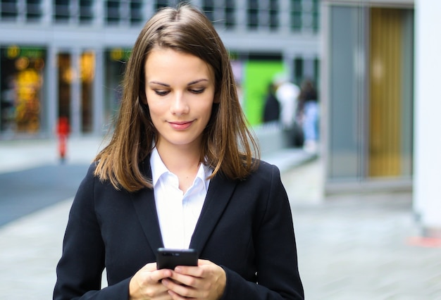 Lächelnde Geschäftsfrau, die einen Smartphone im Freien verwendet