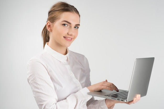 Lächelnde Geschäftsfrau im weißen Hemd, das Laptop hält und während die Kamera stehen und betrachten