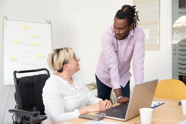 Lächelnde Geschäftsfrau mit Behinderung sitzt im Rollstuhl vor Laptop-Meeting mit Geschäftspartner