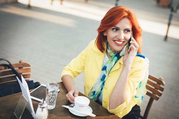 Lächelnde Geschäftsfrau mit Telefon auf einer Kaffeepause in einem Straßencafé.