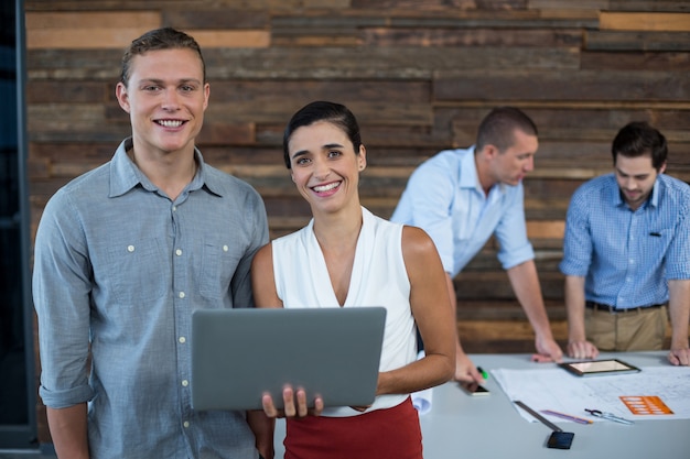 Lächelnde Geschäftsleiter, die im Büro mit Laptop stehen