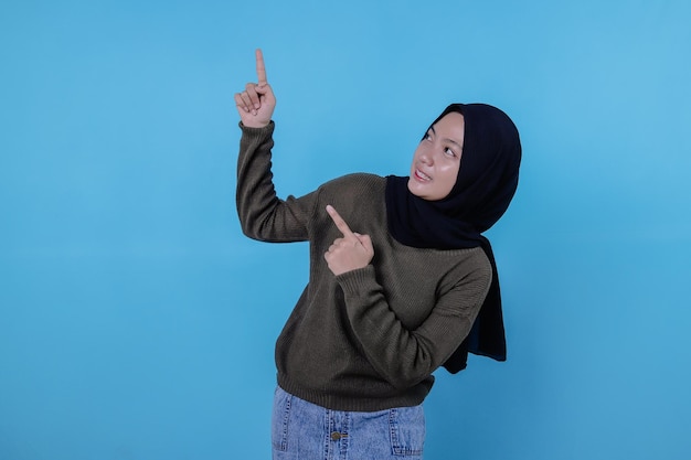 Lächelnde glückliche asiatische Frau mit ihrem Fingerzeig lokalisiert auf hellblauem Fahnenhintergrund
