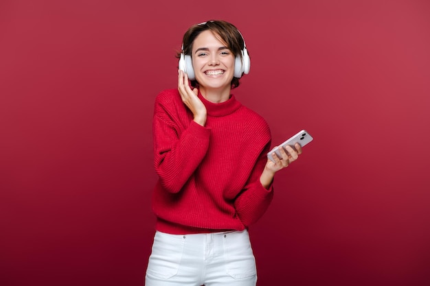 Lächelnde, glückliche junge Frau mit rotem Rollhals hört Musik in Kopfhörern