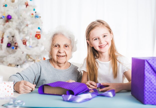 Lächelnde Großmutter mit kleinen Enkelin decken Geschenke mit dekorativem Papier ab