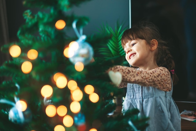 Lächelnde hängende Verzierungen des kleinen Mädchens auf einem Weihnachtsbaum