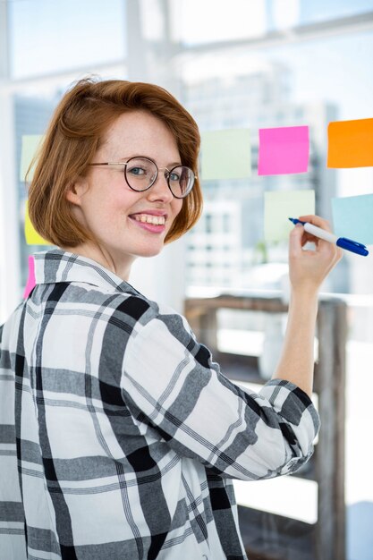 Lächelnde hippie-frau, die anmerkungen auf einer anschlagtafel im büro haftet