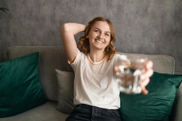 Lächelnde hübsche Frau hält zu Hause ein Glas Wasser