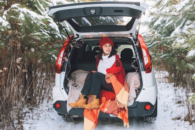 Lächelnde hübsche Frau im Kofferraum im verschneiten Winterwaldkopierraum