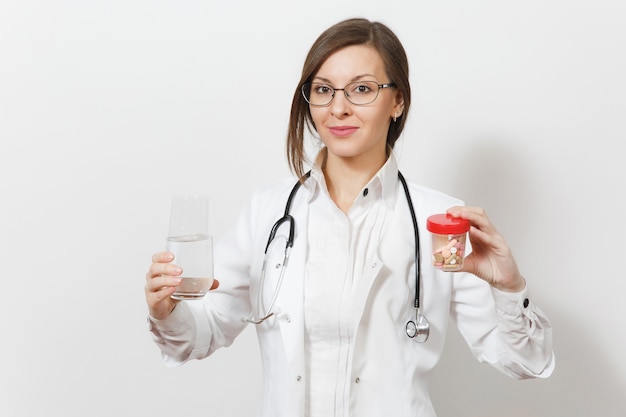 Lächelnde hübsche junge Doktorfrau mit Stethoskop, Brille isoliert auf weißem Hintergrund. Ärztin im medizinischen Kittel hält Flasche mit Pillen, Glas Wasser. Gesundheitspersonal, Medizinkonzept.