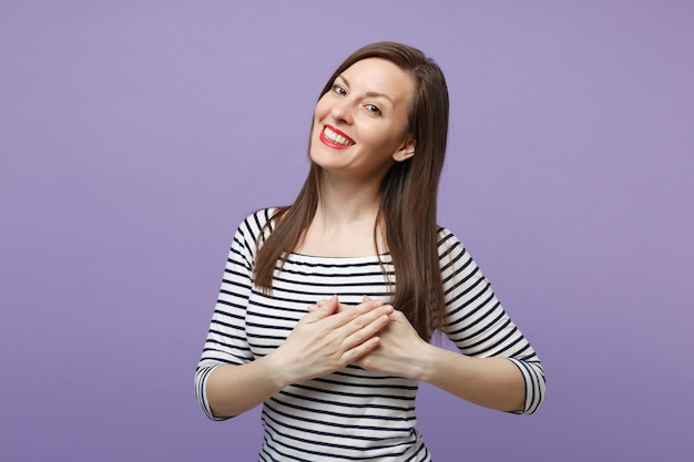 Lächelnde hübsche junge Frau in lässig gestreifter Kleidung, die isoliert auf violettem, violettem Hintergrund Studioporträt posiert. People-Lifestyle-Konzept. Mock-up-Kopienbereich. Halten Sie die Hände auf der Brust gekreuzt, Herz.