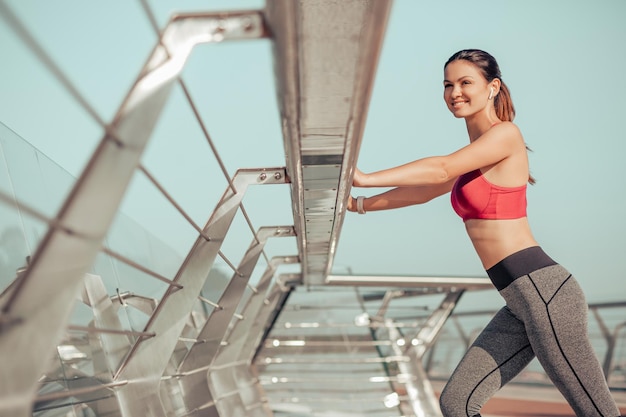 Lächelnde Joggerin, die sich vor dem Training auf der Stadtbrücke aufwärmt