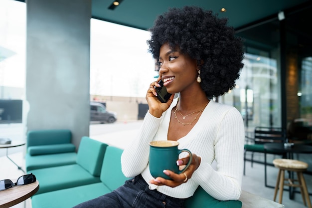 Lächelnde junge afrikanische Frau, die auf Mobiltelefon am Café spricht