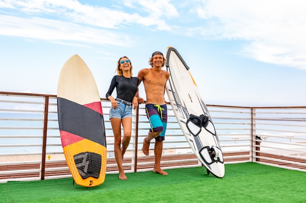 Lächelnde junge aktive Paarsurfer, die auf dem Strand nach Sport mit Surfbrett sich entspannen. Gesunder Lebensstil. Extremer Wassersport